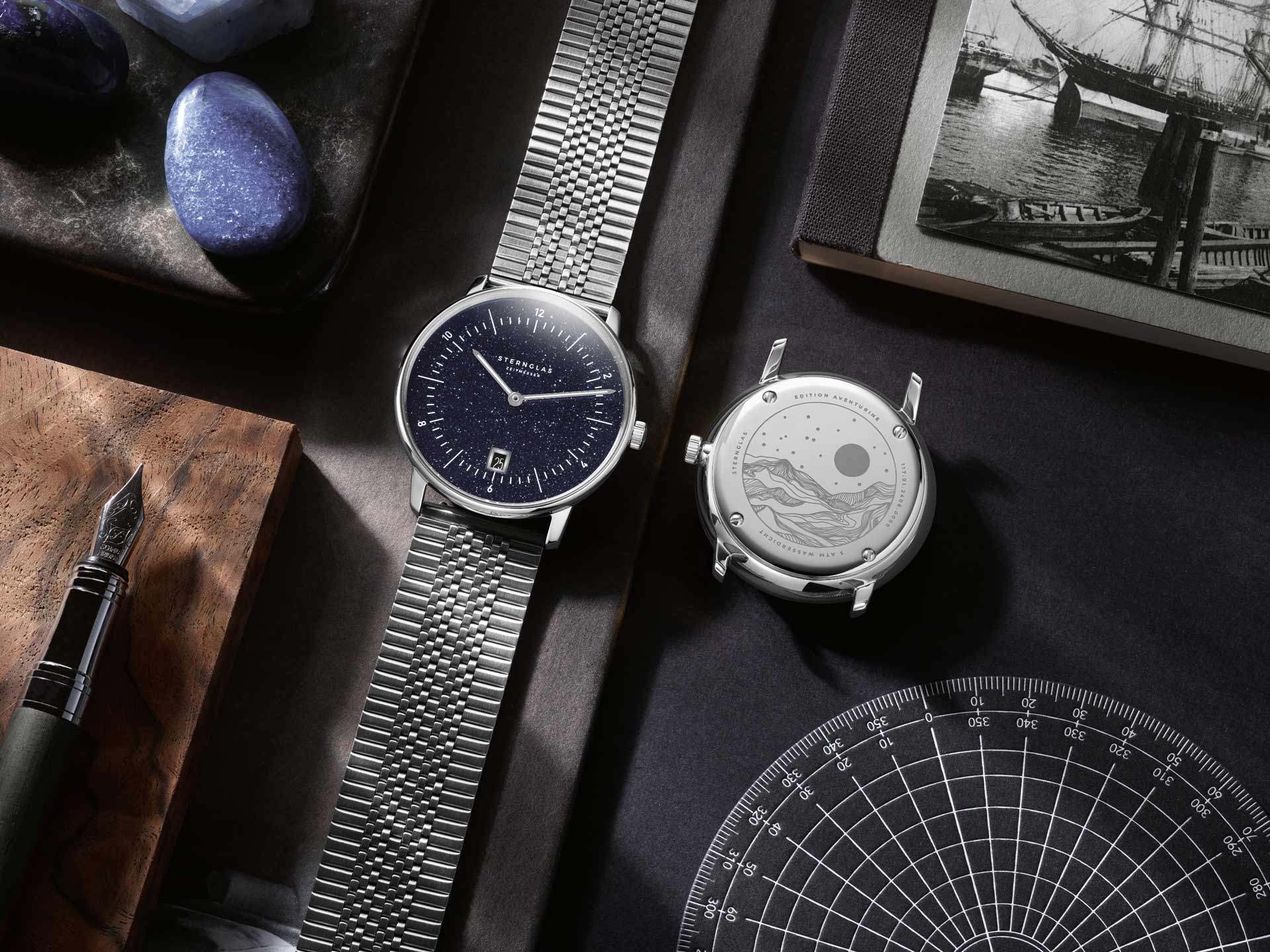 Zwei silberne Armbanduhren liegen nebeneinander auf einem Schreibtisch mit maritimen Motiven